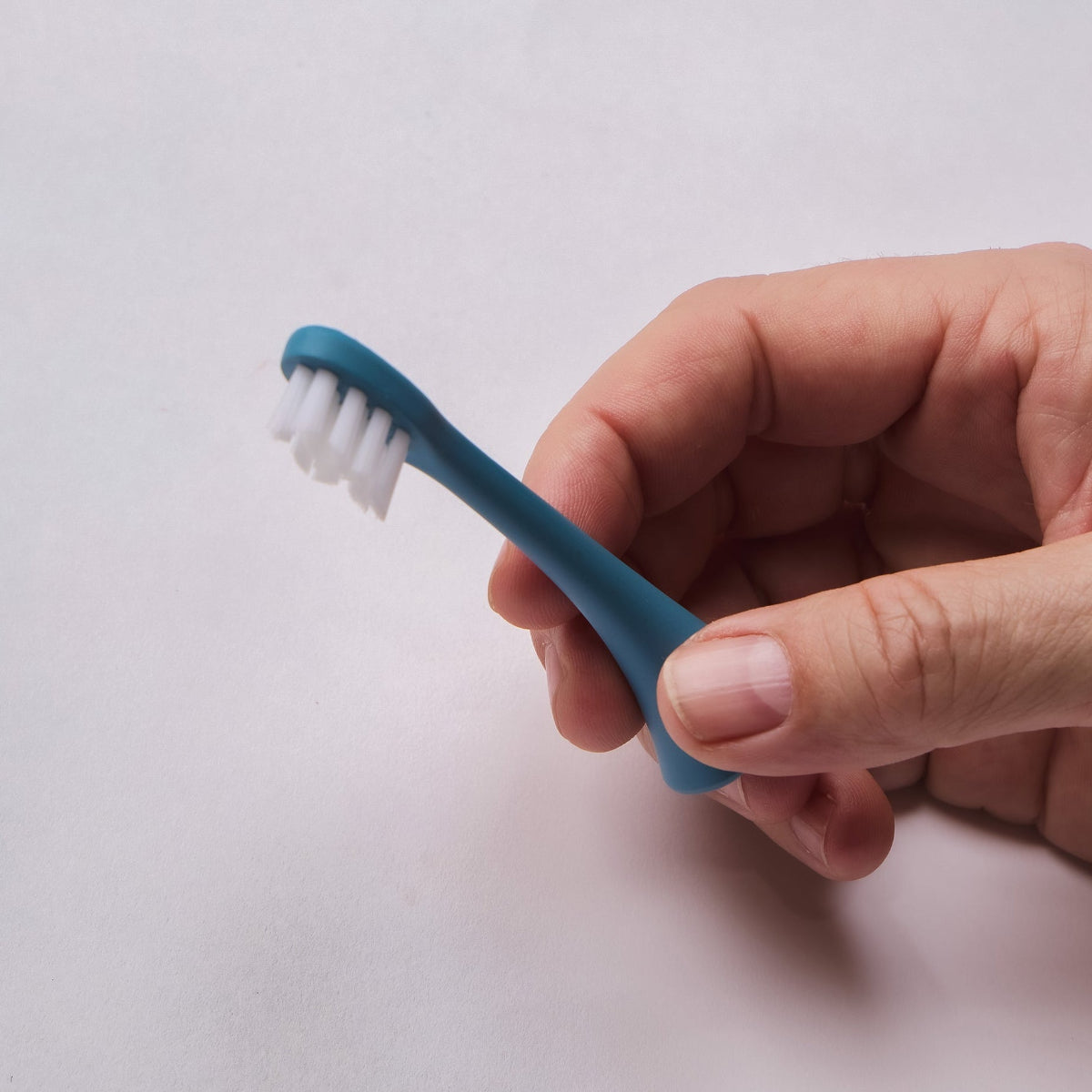 Hand holding a Sapphire Blue Bepulo Next replacement brush head with white bristles.