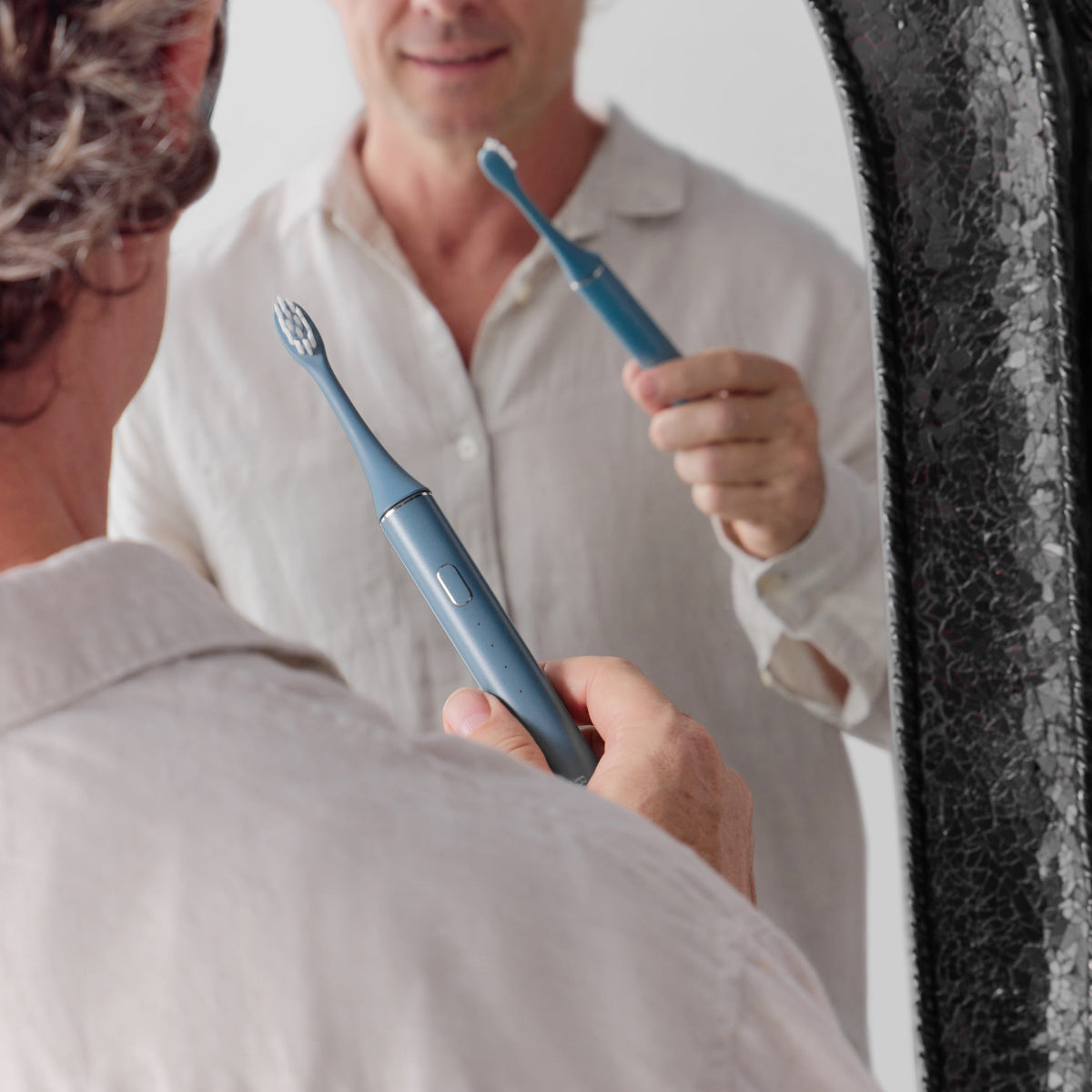 Man in a bathroom holding a sapphire blue Bepulo Next sonic electric toothbrush in front of a mirror. #colour_sapphire blue