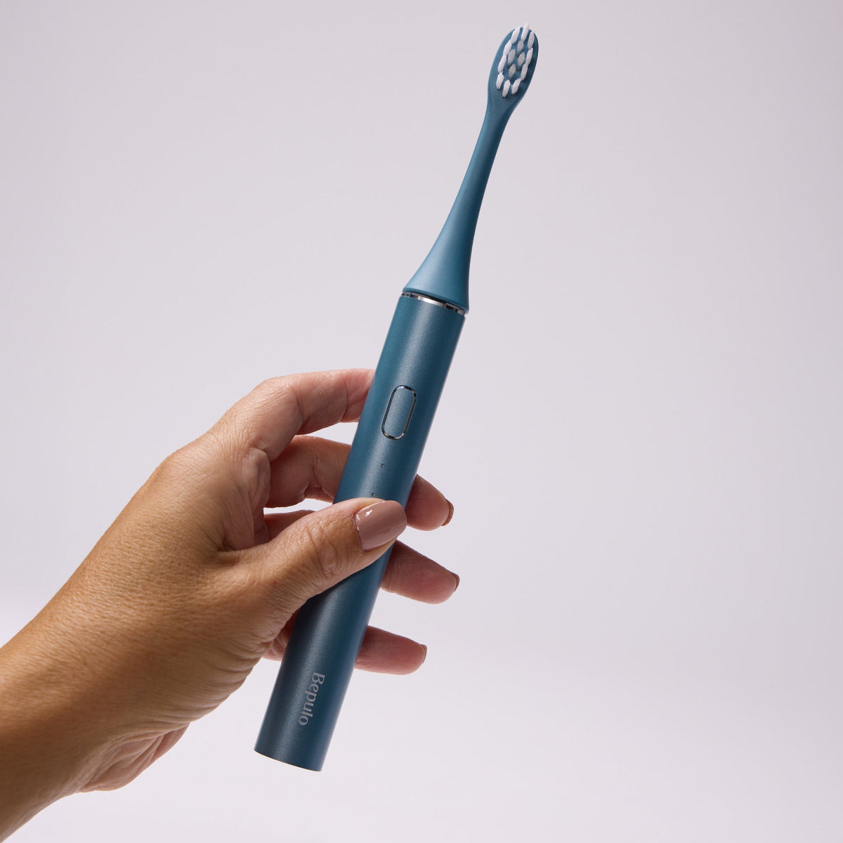 Hand holding a sapphire blue Bepulo Next sonic electric toothbrush against a grey background. #colour_sapphire blue