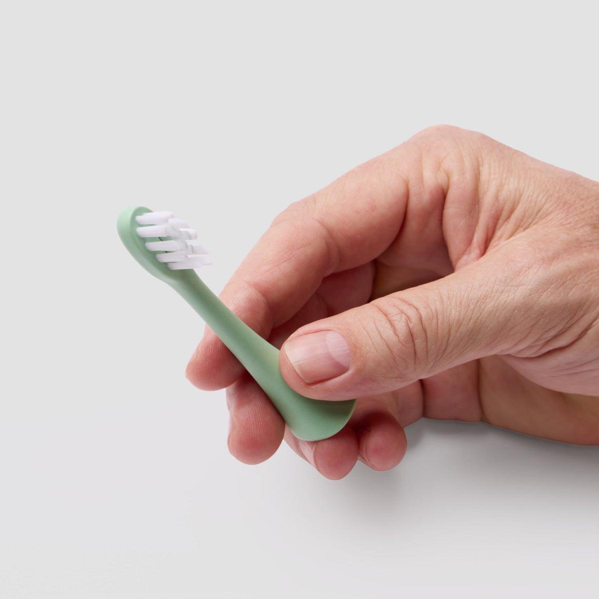 A hand holding a Bepulo green toothbrush head with white bristles against a plain light gray background. #colour_pistachio green