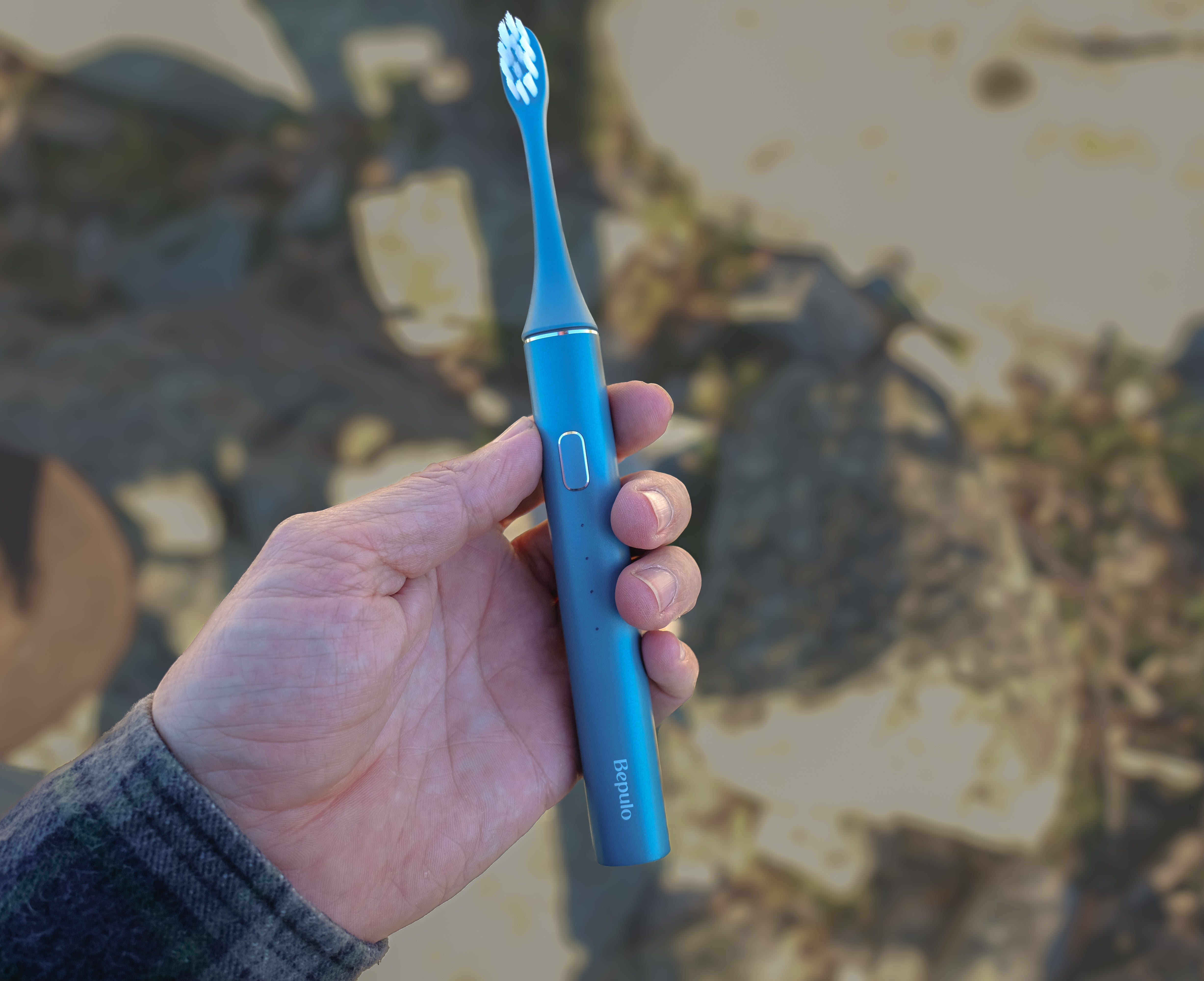 Hand holding a blue electric toothbrush with a blurred background