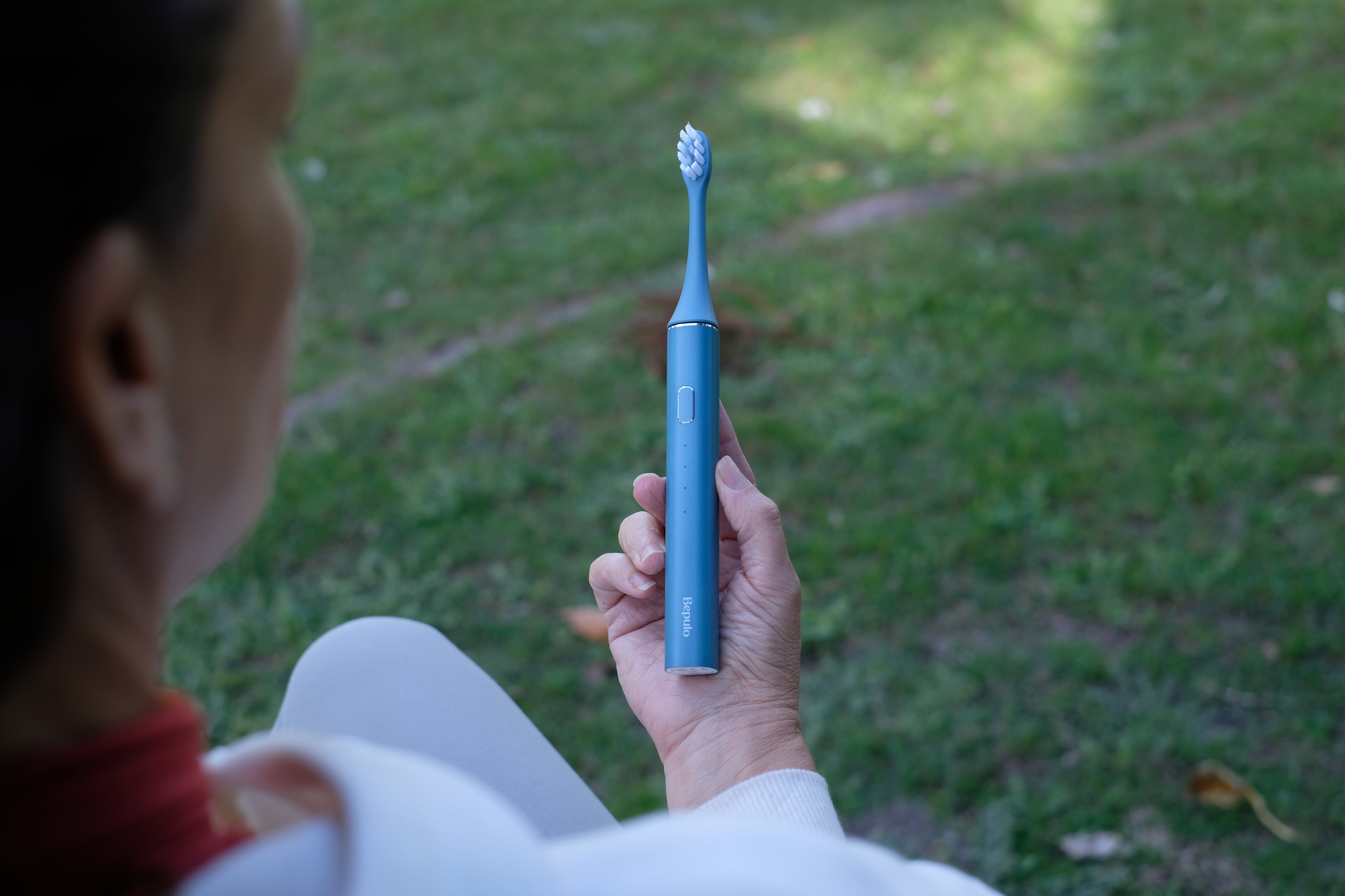 Person holding a blue electric toothbrush outdoors