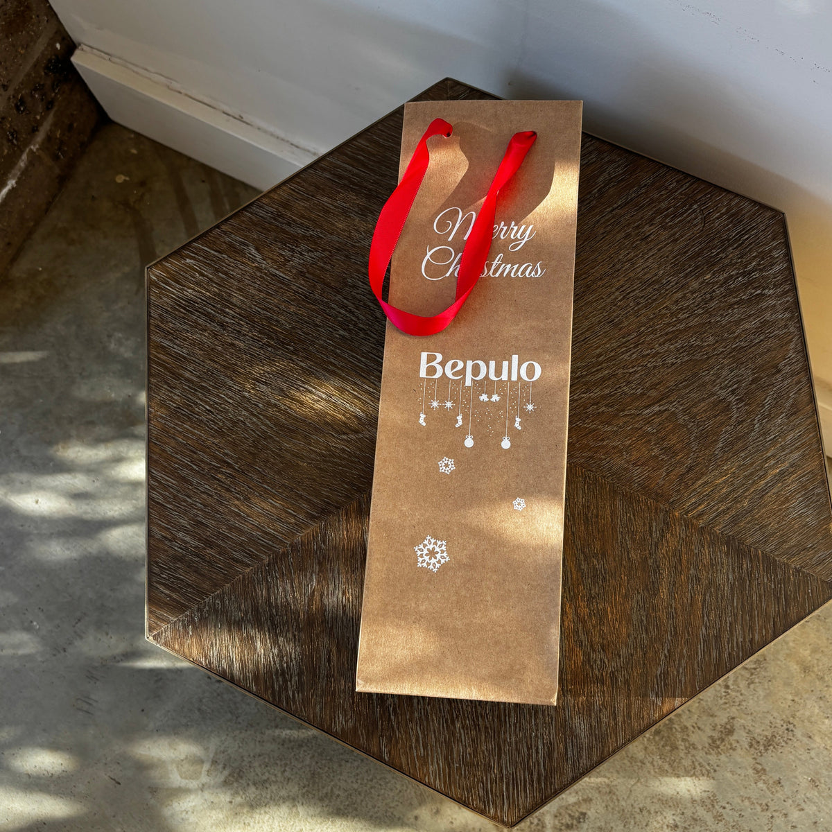 A xmas gift bag with Bepulo written on it, laying on a small table