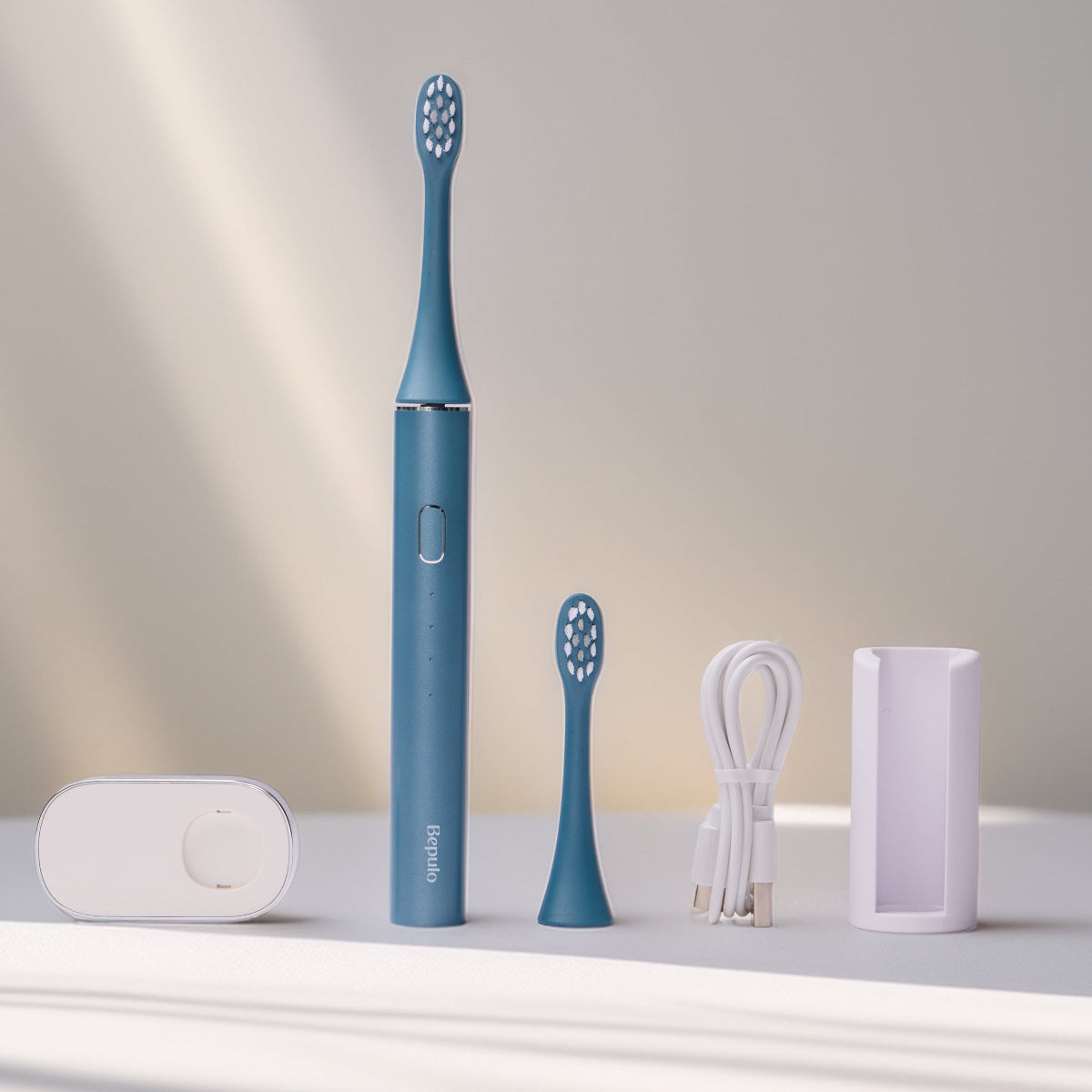 Bepulo Next sapphire blue sonic electric toothbrush shown with standalone bathroom accessories including replacement heads and wall holder. #colour_sapphire blue