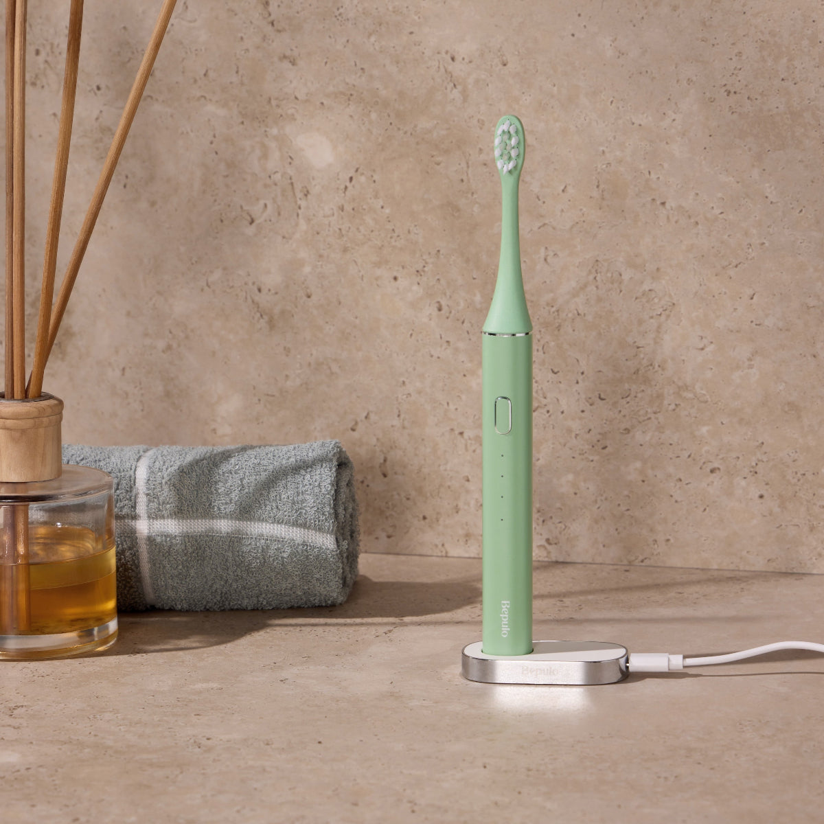 Bepulo Next pistachio green sonic electric toothbrush charging on its magnetic base with bathroom accessories in the background. #colour_pistachio green