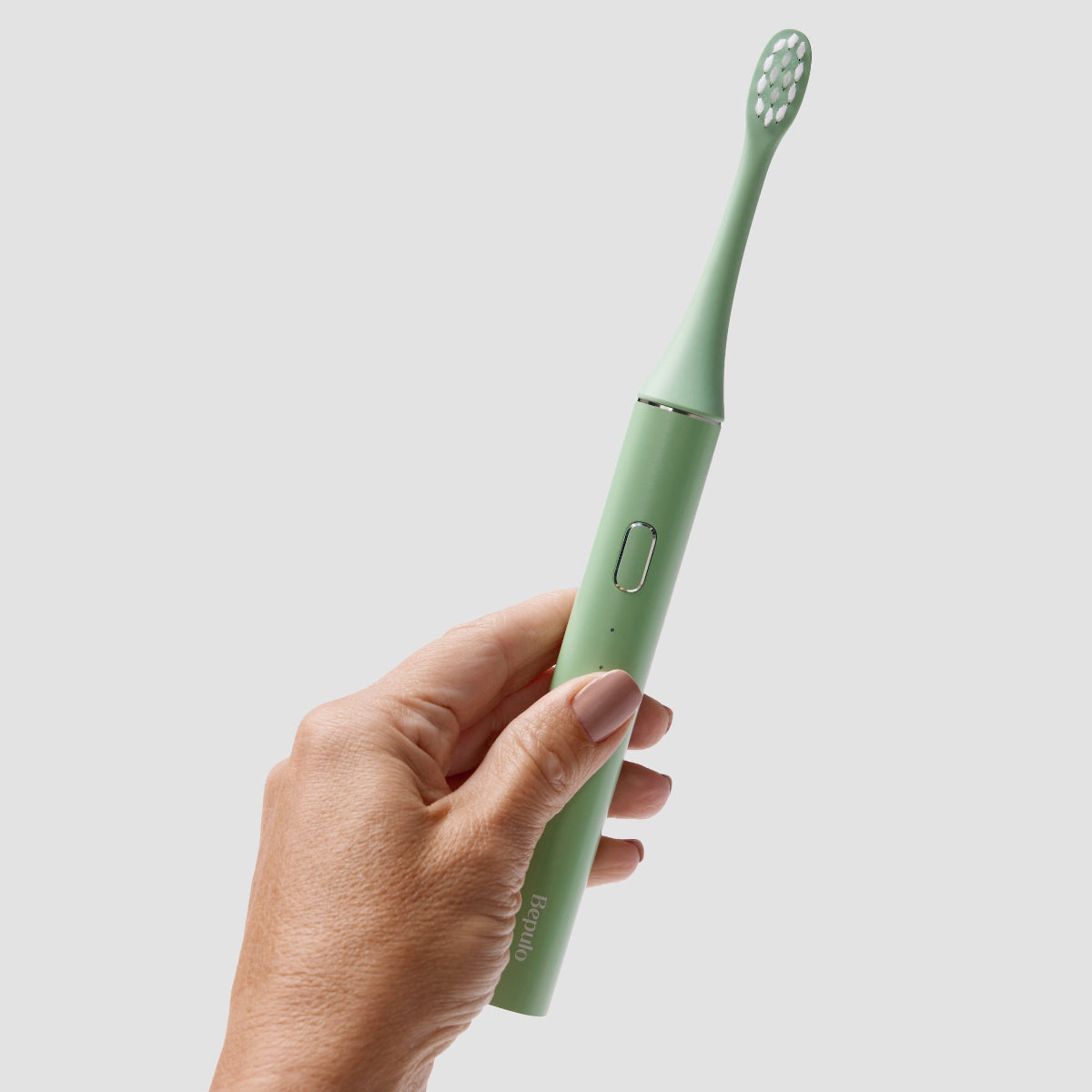 Hand holding a Bepulo Next pistachio green sonic electric toothbrush against a light grey background. #colour_pistachio green