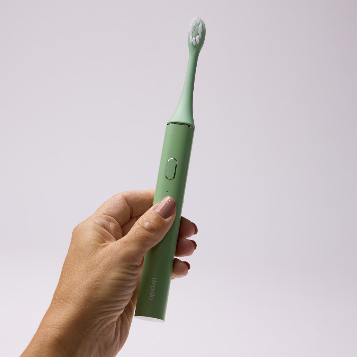 Hand holding a pistachio green Bepulo Next sonic electric toothbrush against a grey background. #colour_pistachio green