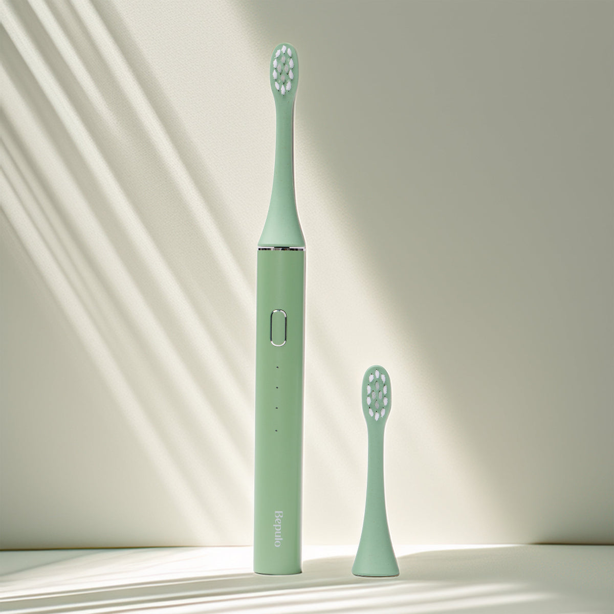 Pistachio green Bepulo Next sonic electric toothbrush standing upright with a replacement brush head on a light grey surface. #colour_pistachio green 
