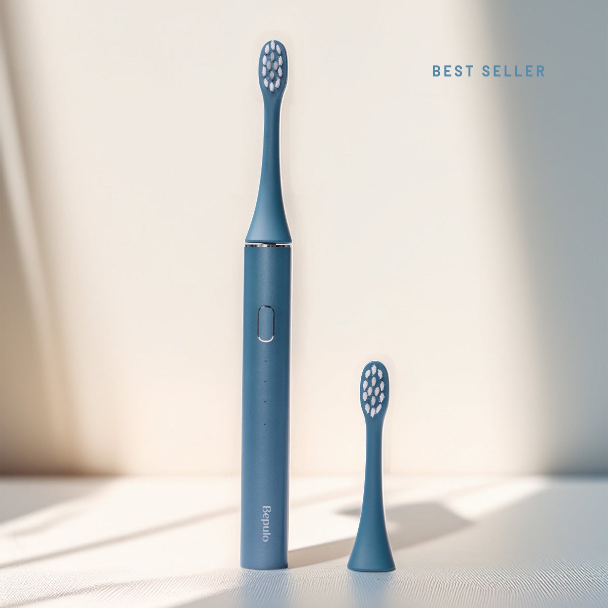 Sapphire Blue Bepulo Next sonic electric toothbrush standing upright next to a replacement brush head. #colour_sapphire blue