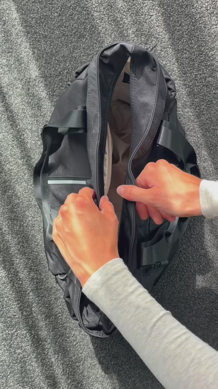 Close-up of hands unzipping the main compartment of a black Bepulo travel duffle bag.