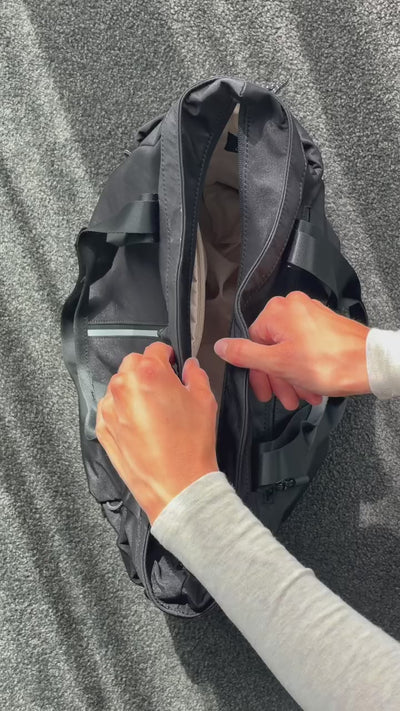 Close-up of hands unzipping the main compartment of a black Bepulo travel duffle bag.